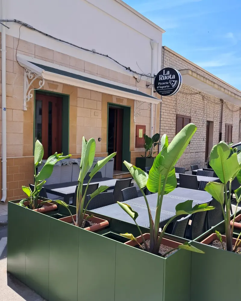 I tavoli all'aperto davanti al locale, fra le fioriere verdi, sotto l'insegna tonda