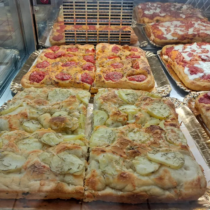 Teglie di pizza e focaccia tagliate a quadrotti nella vetrina